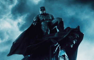 A Man In A Batman Costume Is Sitting On A Statue GIF