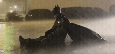 A Man In A Batman Costume Is Sitting On Top Of Another Man In A Puddle Of Water . GIF
