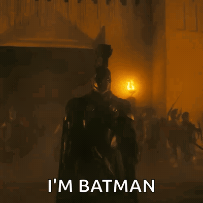 A Man In A Batman Costume Is Standing In Front Of A Group Of People . GIF