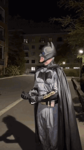 A Man In A Batman Costume Is Walking Down The Street GIF