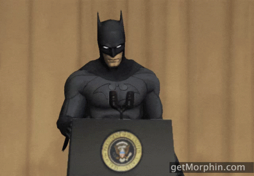 A Man In A Batman Costume Stands At A Podium With A Microphone In His Hand GIF