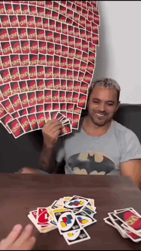 A Man In A Batman Shirt Is Playing Uno GIF