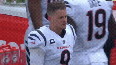 A Man In A Bengals Jersey Is Kneeling Down On The Field . GIF