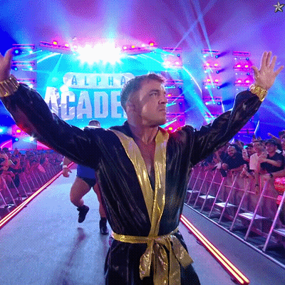 A Man In A Black And Gold Robe Stands In Front Of A Stage That Says Alpha Arcade GIF