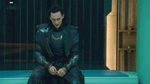 A Man In A Black And Green Costume Is Sitting On A Bench GIF