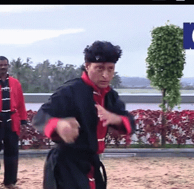 A Man In A Black And Red Karate Uniform Stands In Front Of A Sign That Says ' Ntv ' GIF