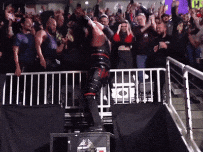 A Man In A Black And Red Outfit Is Jumping Over A Fence In Front Of A Crowd With A Yellow Sign That Says Ps GIF