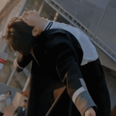 A Man In A Black And White Jacket Is Bending Over In Front Of A Building . GIF