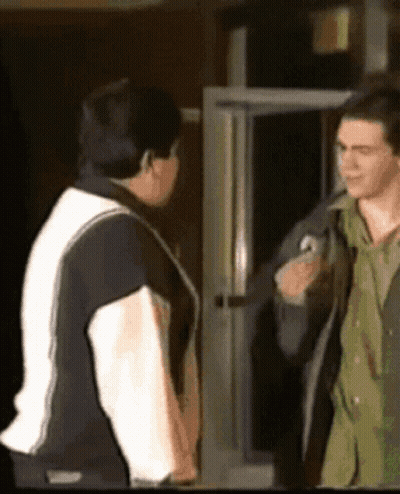 A Man In A Black And White Jacket Is Talking To Another Man GIF