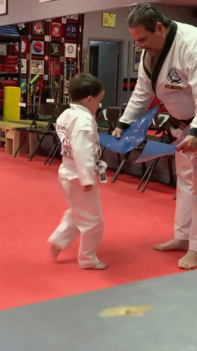 A Man In A Black And White Karate Uniform Is Teaching A Little Boy GIF