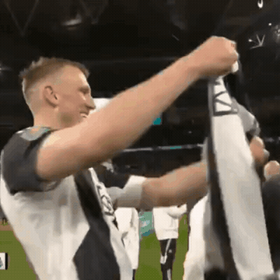 A Man In A Black And White Shirt Holds Up A Scarf With The Letter A On It GIF