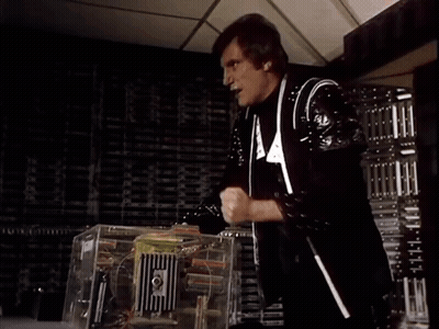 A Man In A Black And White Suit Is Standing In Front Of A Machine And Says Damn It GIF