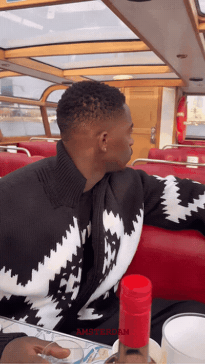 A Man In A Black And White Sweater Sits On A Boat With The Word Amsterdam On The Bottom GIF
