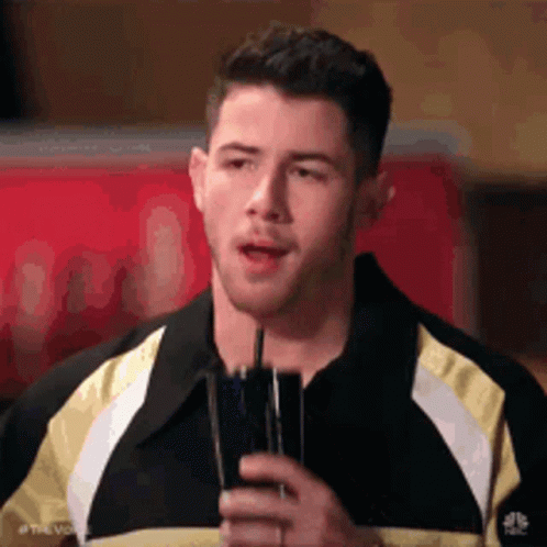 A Man In A Black And Yellow Jacket Is Holding A Glass Of Water . GIF