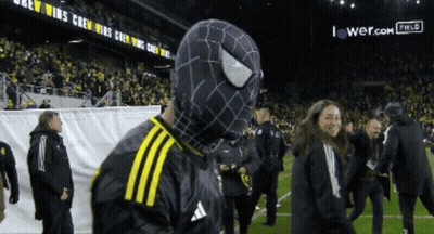 A Man In A Black And Yellow Spider Man Costume Stands On A Field GIF