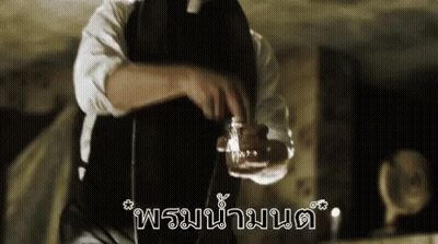 A Man In A Black Apron Is Holding A Glass Of Liquid In His Hand . GIF