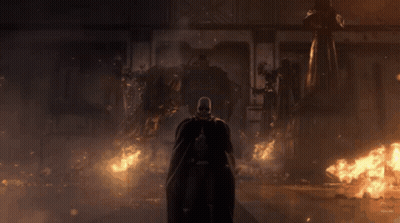 A Man In A Black Cape Is Standing In Front Of A Burning Building GIF