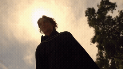 A Man In A Black Cape Stands In Front Of A Tree With The Sun Shining Through It GIF