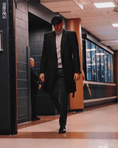 A Man In A Black Coat And Hat Walks Down A Hallway With A Sign That Says Cnn On It GIF