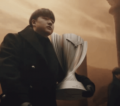 A Man In A Black Coat Holds A Silver Trophy GIF