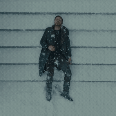 A Man In A Black Coat Is Laying On The Ground In The Snow GIF