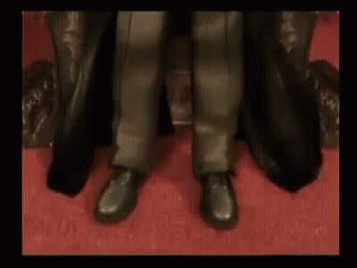 A Man In A Black Coat Is Sitting In A Chair . GIF