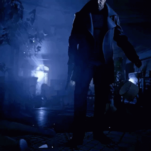 A Man In A Black Coat Is Standing In A Dark Room Holding A Gun GIF