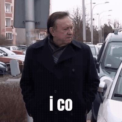A Man In A Black Coat Is Standing In A Parking Lot With His Hands In His Pockets And The Words I Co On His Chest GIF