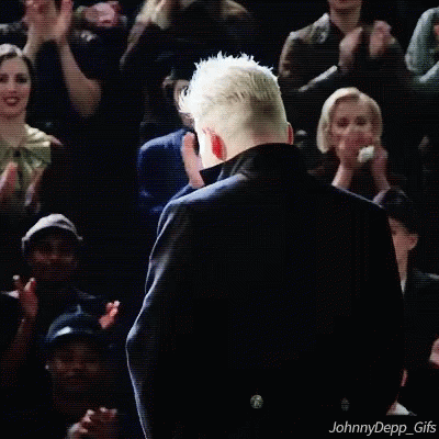 A Man In A Black Coat Is Standing In Front Of A Crowd Of People . GIF