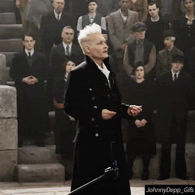 A Man In A Black Coat Is Standing In Front Of A Crowd Of People . GIF