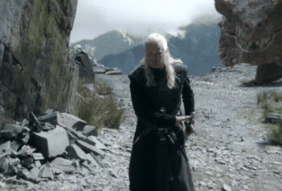 A Man In A Black Coat Is Standing In Front Of A Large Dragon GIF