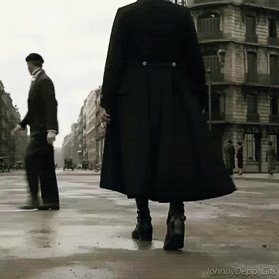 A Man In A Black Coat Is Walking Down A Wet Street GIF