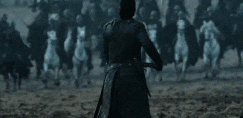 A Man In A Black Coat Stands In Front Of A Crowd Of Horses With His Arms Outstretched GIF
