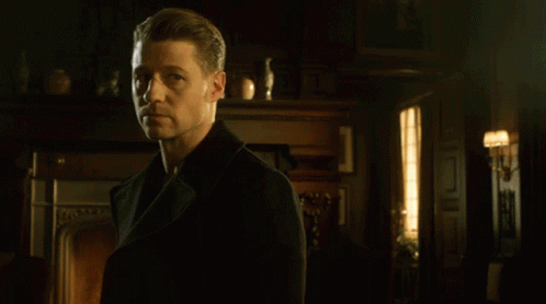 A Man In A Black Coat Stands In Front Of A Fireplace In A Dark Room GIF