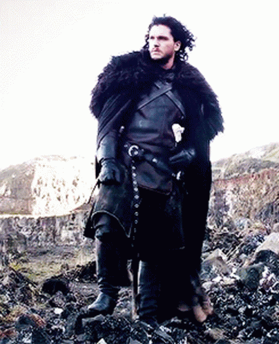A Man In A Black Costume Is Standing On A Rocky Hillside Holding A Sword . GIF