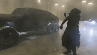 A Man In A Black Dress Is Dancing In Front Of A Car . GIF