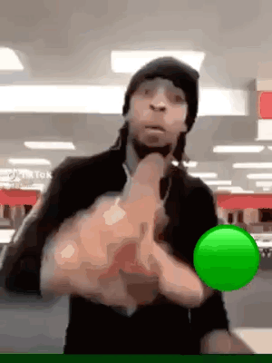 A Man In A Black Hat Is Holding A Green Ball In His Hands . GIF