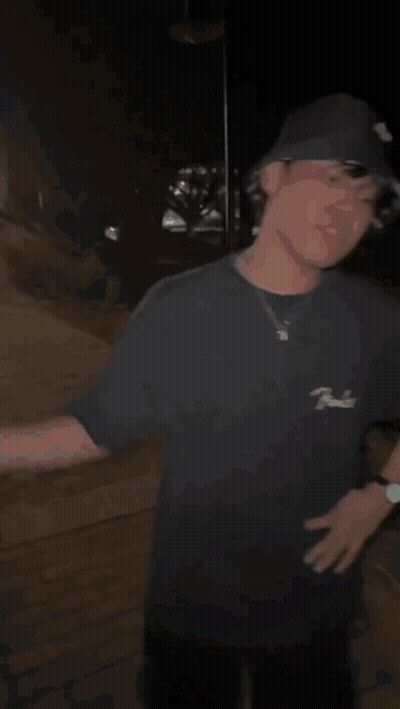A Man In A Black Hat Is Shaking Hands With Another Man In A Dark Room . GIF
