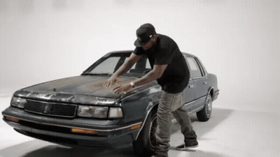 A Man In A Black Hat Is Standing Next To A Car GIF