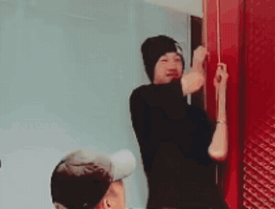 A Man In A Black Hat Is Standing Next To A Red Door . GIF