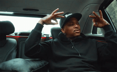 A Man In A Black Hoodie And A Black Hat With The Word Bomb On It Is Sitting In The Back Seat Of A Car GIF
