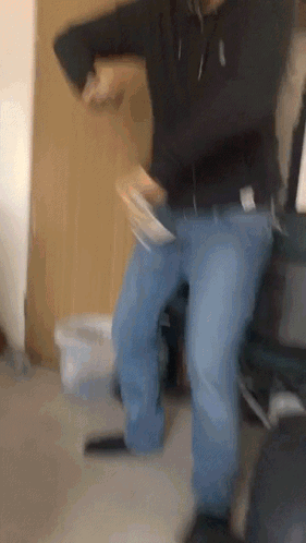 A Man In A Black Hoodie And Blue Jeans Is Dancing In A Room . GIF