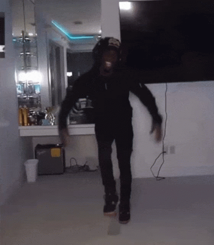 A Man In A Black Hoodie And Hat Is Dancing In A Room GIF