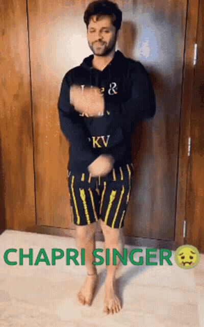 A Man In A Black Hoodie And Yellow Shorts Is Dancing In Front Of A Wall . GIF