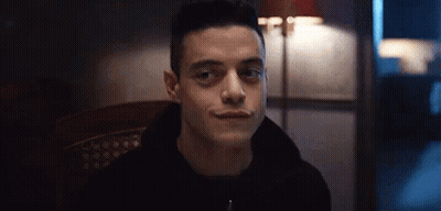 A Man In A Black Hoodie Is Sitting In A Chair And Smiling At The Camera . GIF