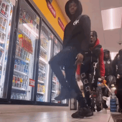 A Man In A Black Hoodie Is Standing In Front Of A Cooler With A Sign That Says Coca Cola On It GIF