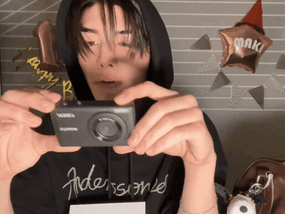 A Man In A Black Hoodie Is Taking A Picture Of Himself With A Kodak Camera GIF
