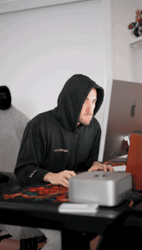 A Man In A Black Hoodie Is Typing On A Laptop GIF