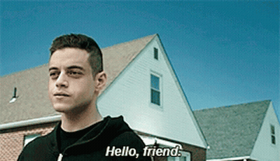 A Man In A Black Hoodie Says Hello Friend In Front Of A House GIF