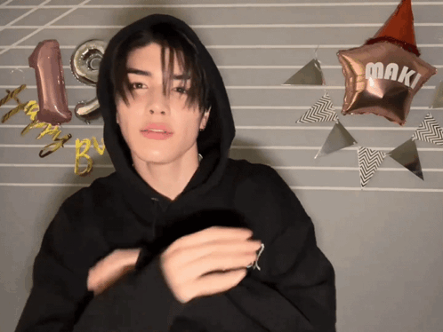 A Man In A Black Hoodie Stands In Front Of Balloons That Say Happy Birthday GIF
